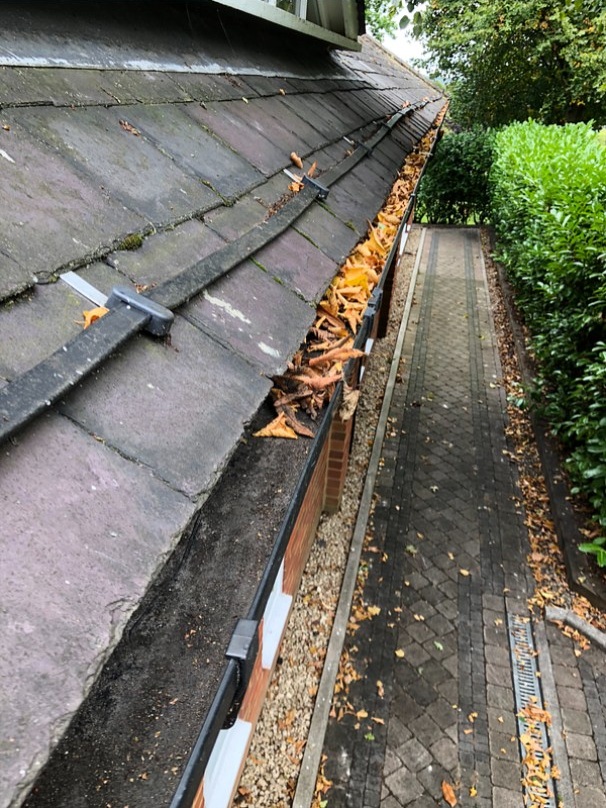 Blocked uPVC gutter filled with autumn leaves during professional gutter clearance